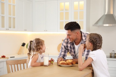 Photo of Little girls and their father eating together at table in modern kitchen