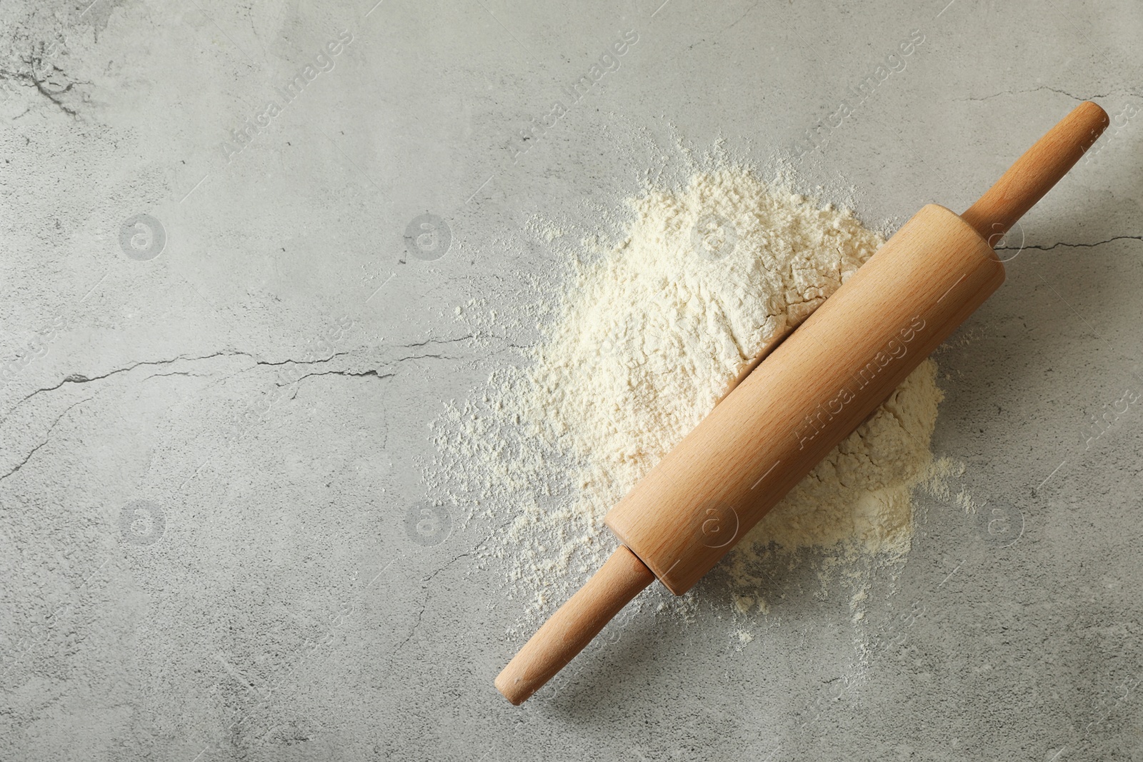 Photo of Flour and rolling pin on grey table, top view. Space for text