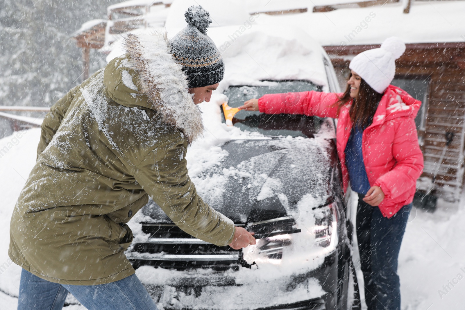 Photo of Young couple cleaning snow from car outdoors on winter day