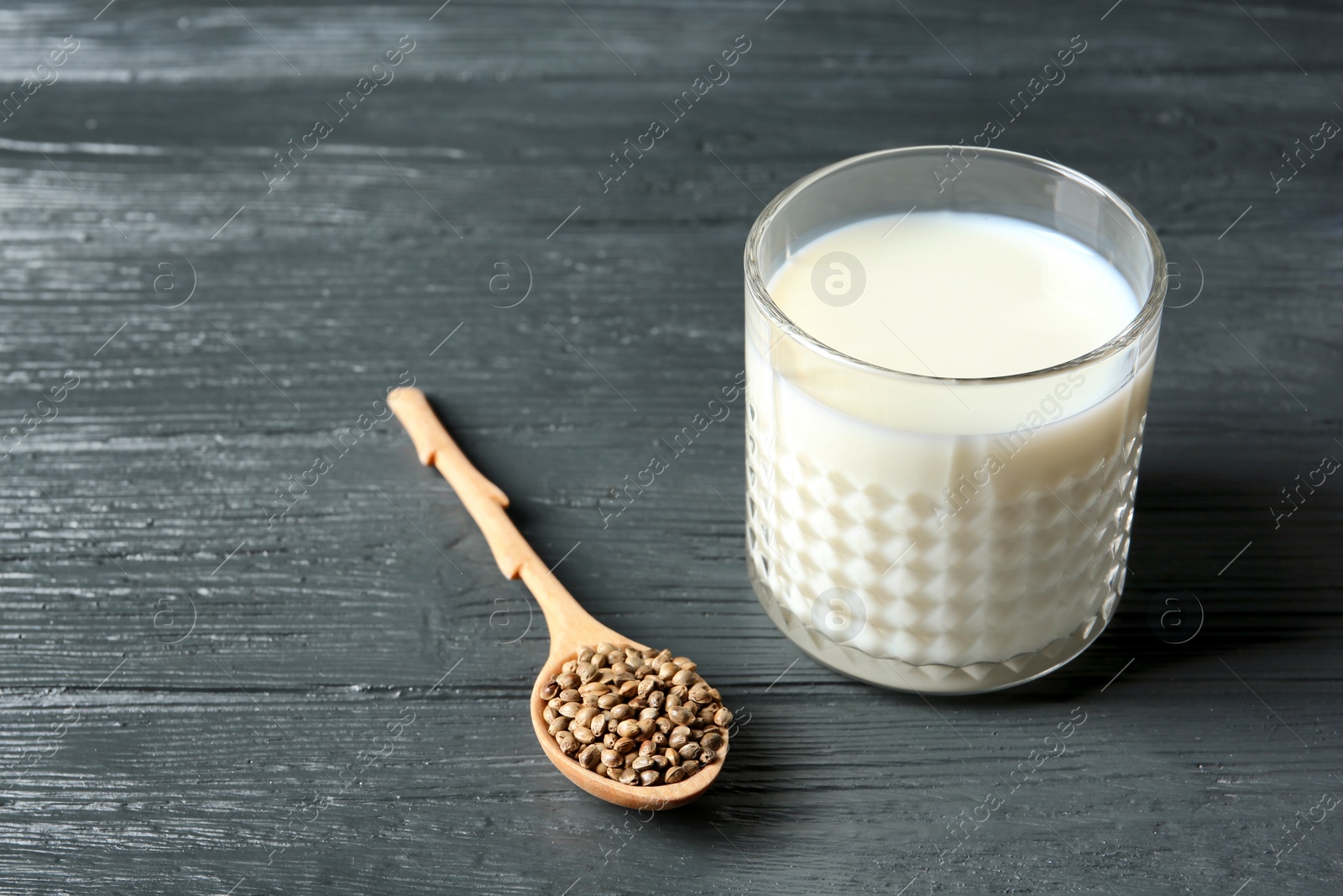 Photo of Glass of hemp milk and spoon with seeds on wooden background