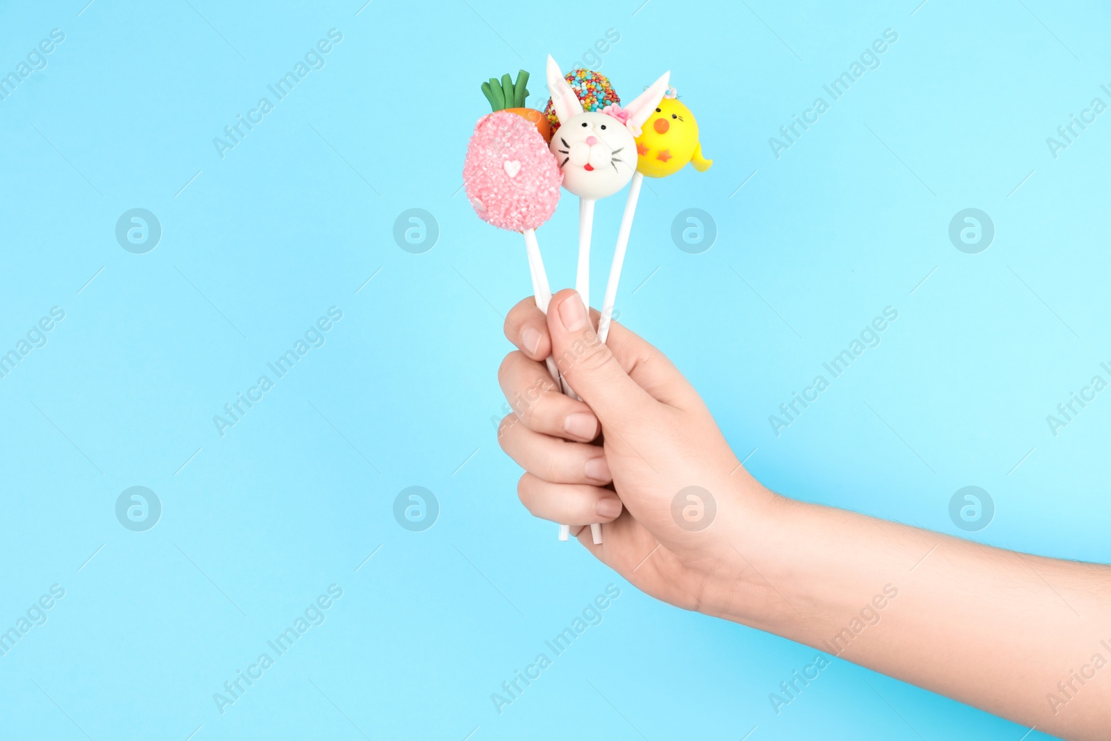 Photo of Woman with delicious cake pops on light blue background, closeup. Easter holiday