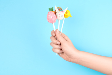 Photo of Woman with delicious cake pops on light blue background, closeup. Easter holiday