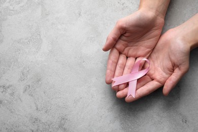 Photo of Woman holding pink ribbon at grey table, top view with space for text. Breast cancer awareness concept