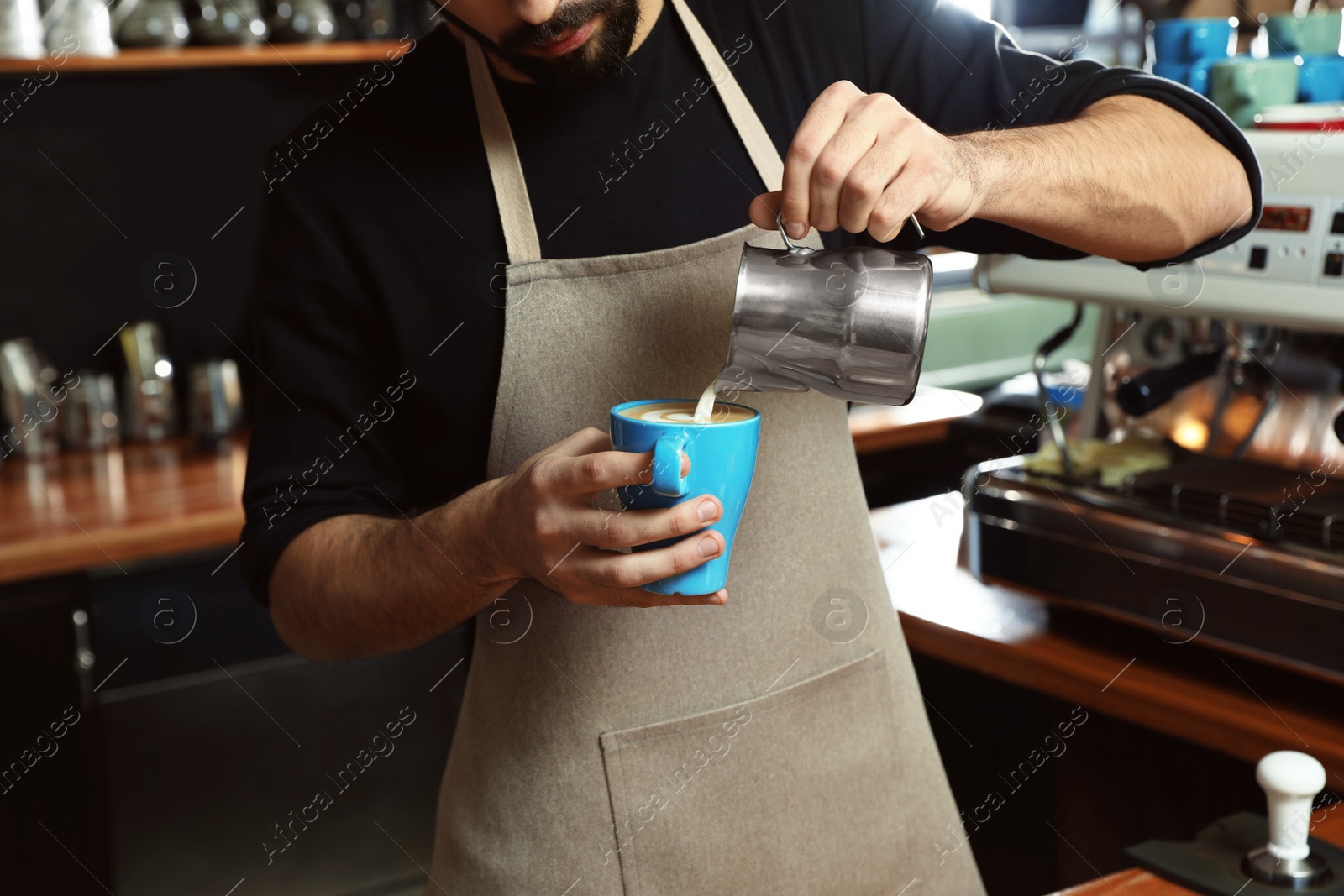Photo of Barista pouring milk into cup of coffee in shop, closeup