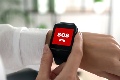 Woman using SOS function on smartwatch indoors, closeup