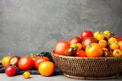 Photo of Fresh ripe tomatoes in wicker bowl on table against grey background. Space for text