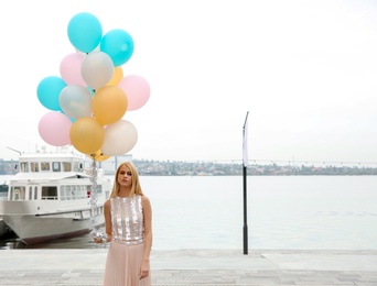 Beautiful young woman with bunch of balloons outdoors. Space for text