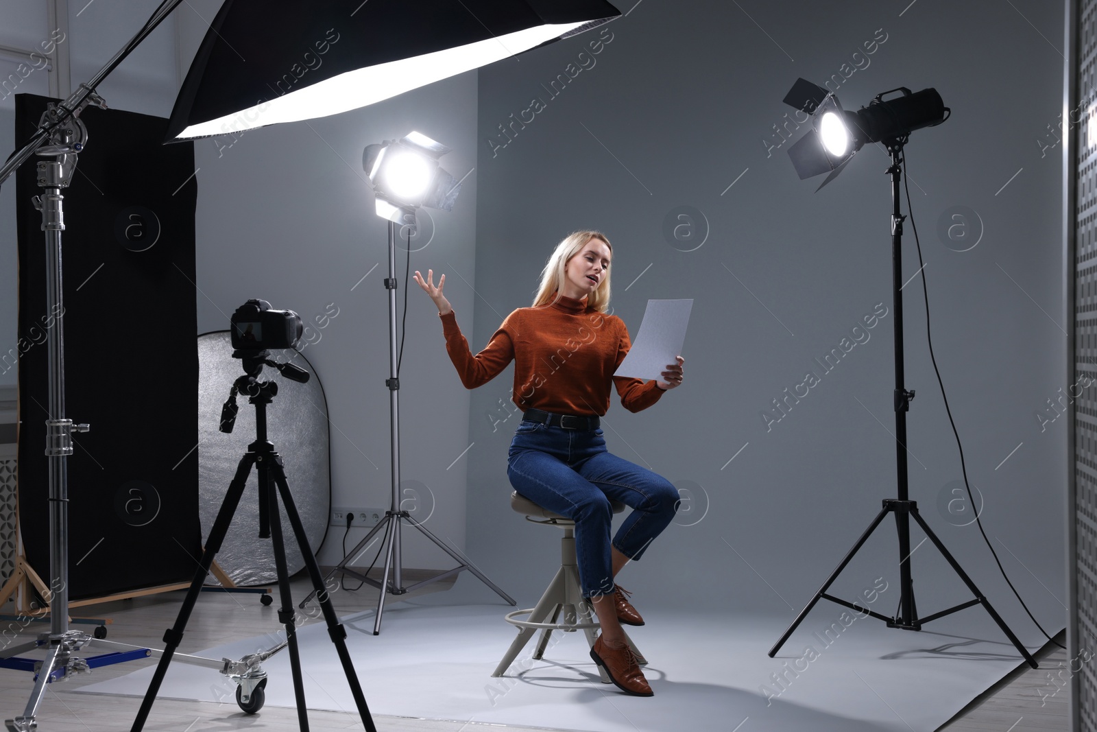 Photo of Casting call. Emotional woman with script sitting on chair and performing in front of camera in studio