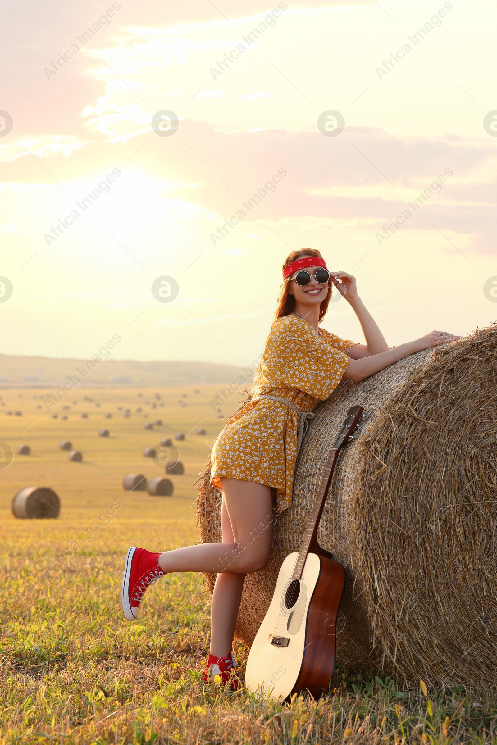 Photo of Happy hippie woman with guitar near hay bale in field, space for text