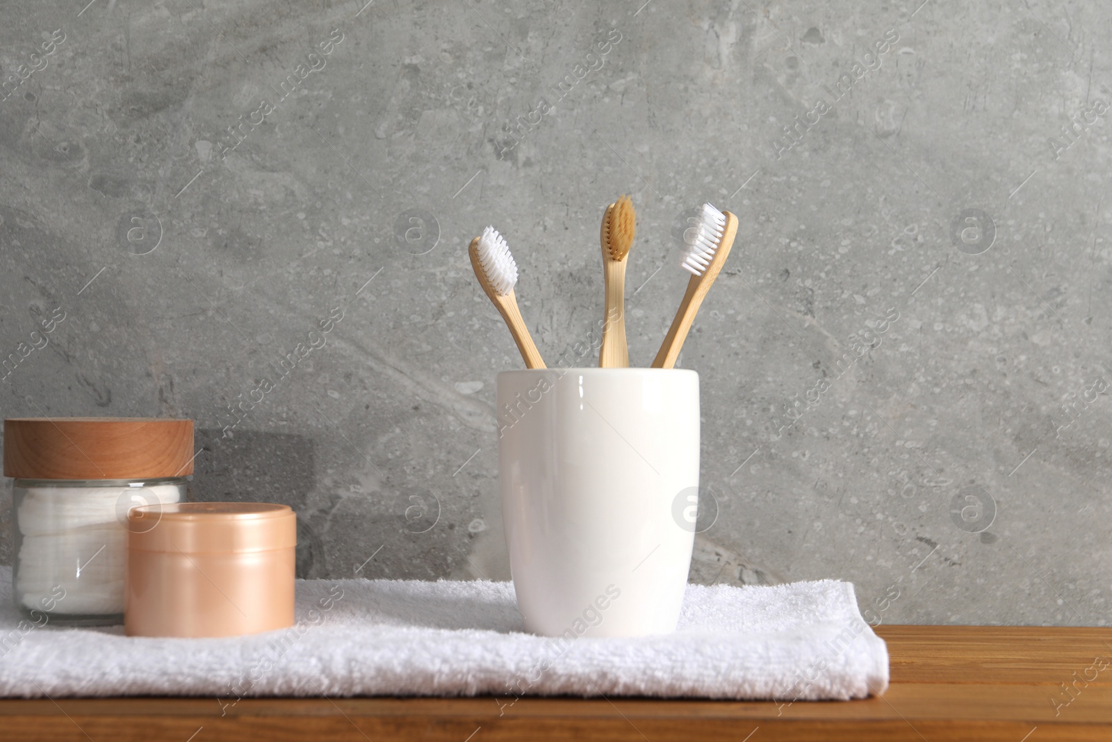 Photo of Bamboo toothbrushes in holder, towel and cosmetic products on wooden table
