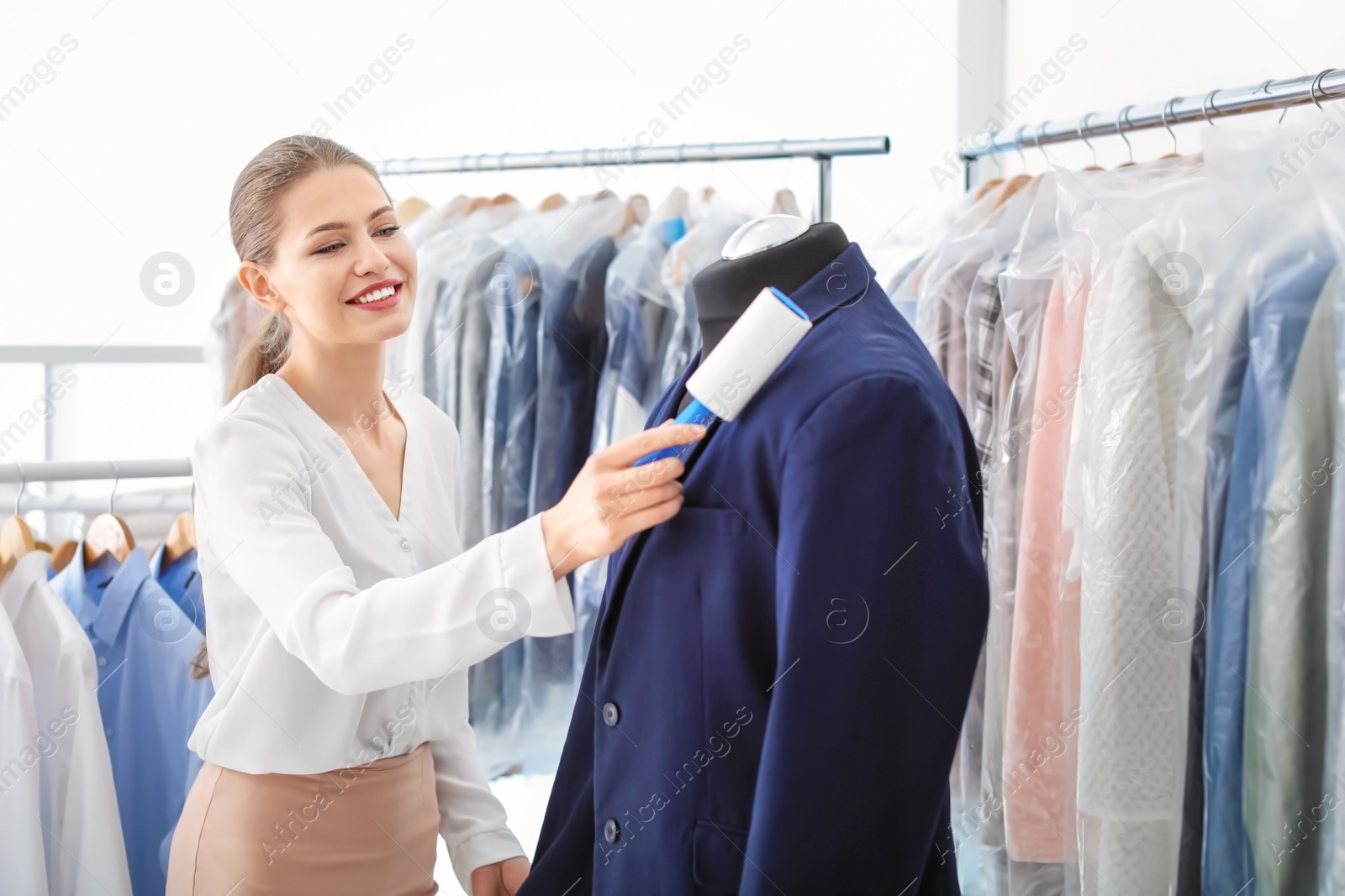 Photo of Young woman removing dust from jacket with lint roller at dry-cleaner's