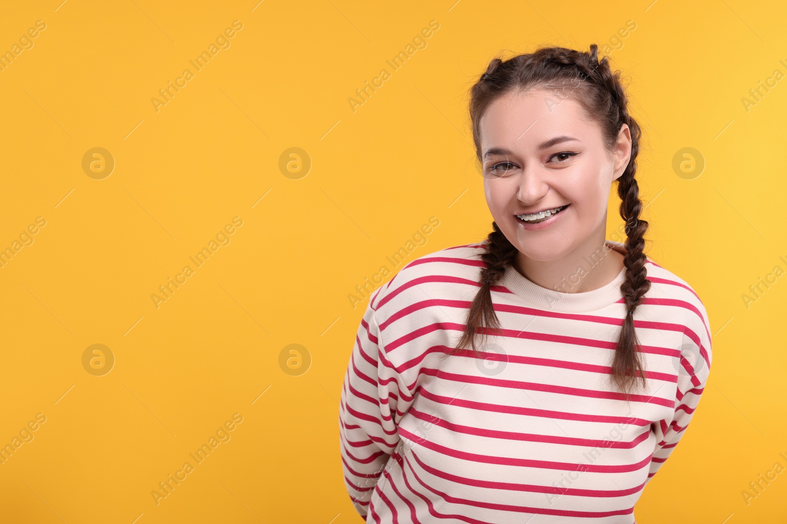 Photo of Smiling woman with braces on orange background. Space for text