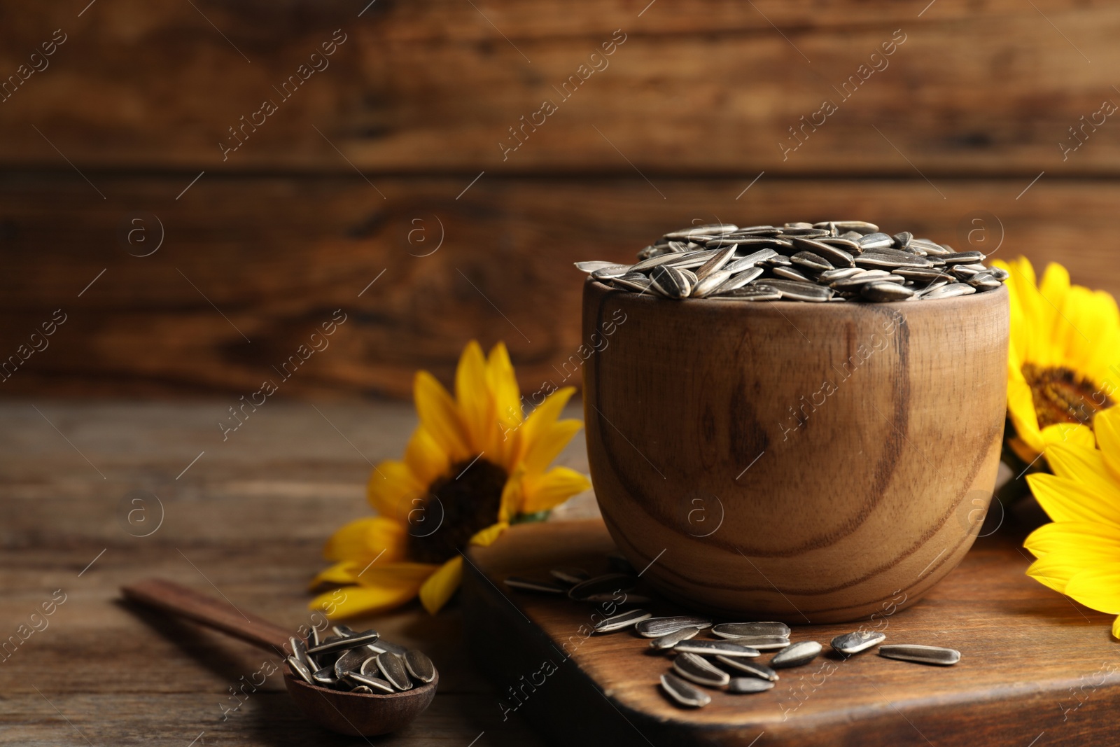 Photo of Raw sunflower seeds and flowers on wooden table. Space for text