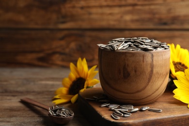 Raw sunflower seeds and flowers on wooden table. Space for text