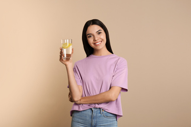 Beautiful young woman with tasty lemon water on beige background