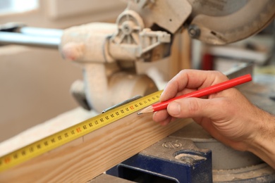 Photo of Working man measuring timber strip in carpentry shop, closeup