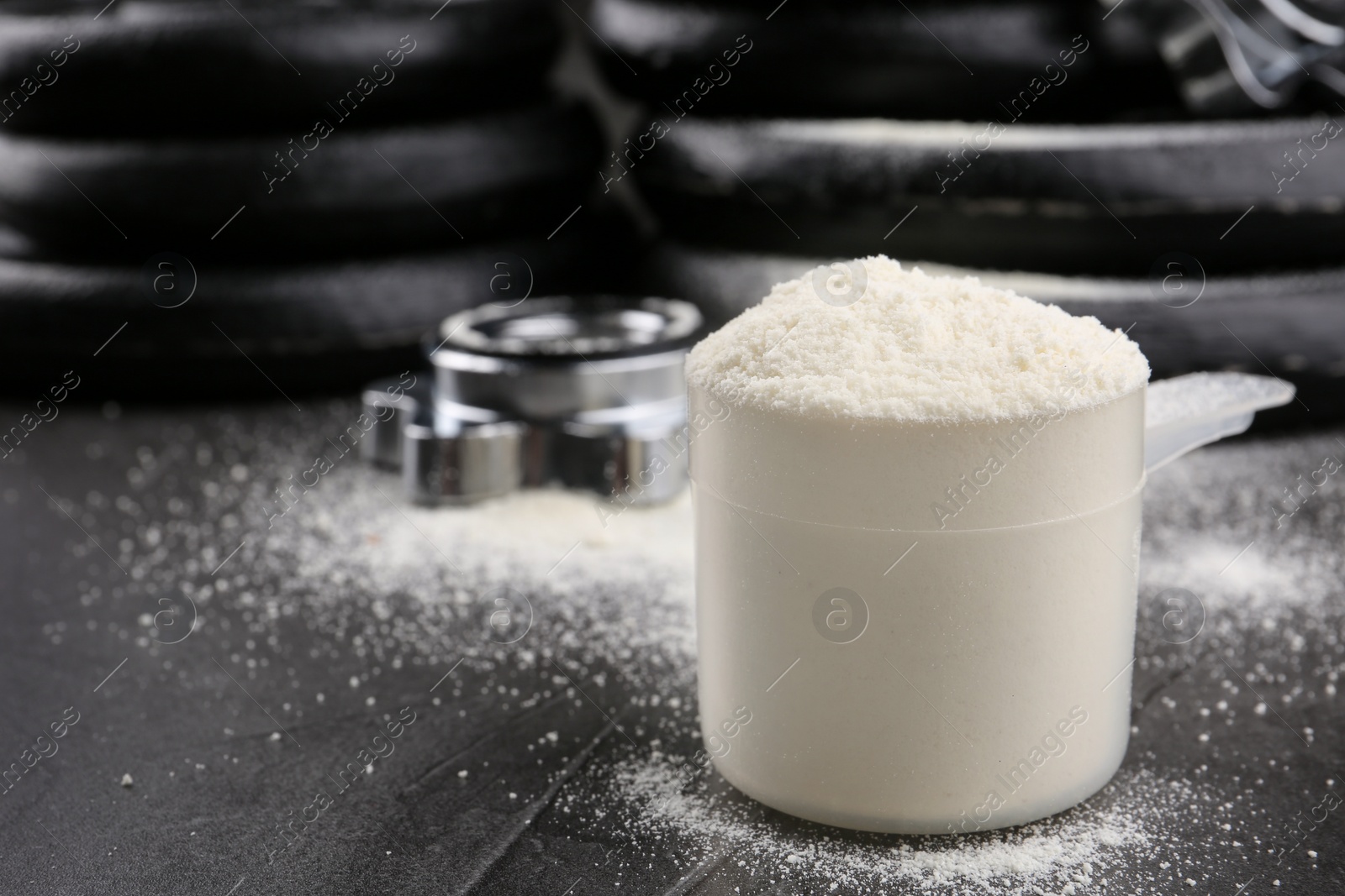 Photo of Measuring scoop of protein powder and weight plates on grey table, closeup