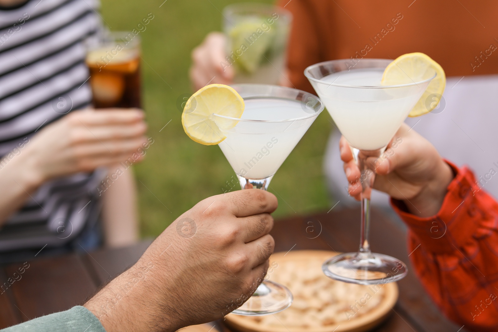 Photo of Friends clinking glasses with cocktails at table outdoors, closeup