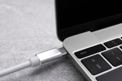 Photo of USB cable with type C connector plugged into laptop port on grey table, closeup