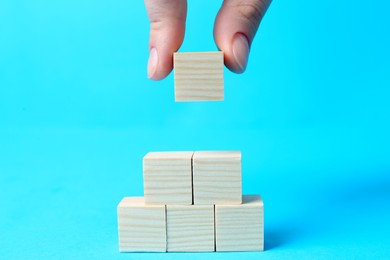 Photo of Woman building pyramid of cubes on light blue background, closeup with space for text. Idea concept