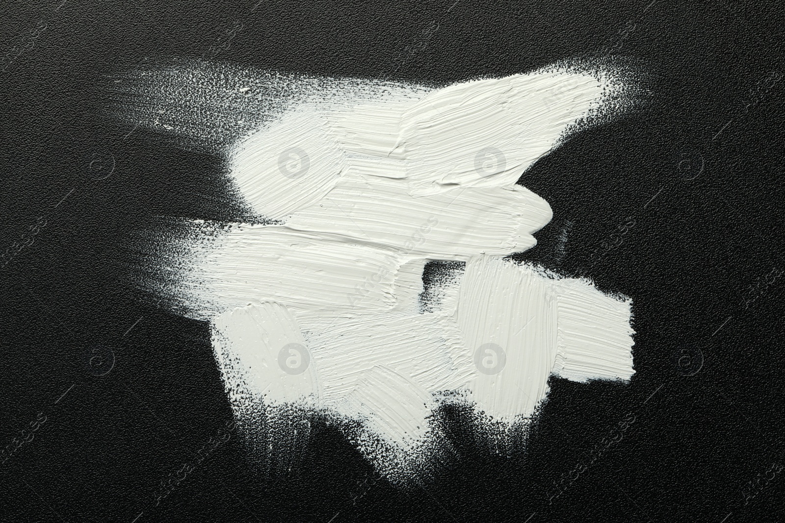 Photo of Strokes of white oil paint on black canvas, top view