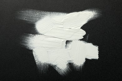 Strokes of white oil paint on black canvas, top view