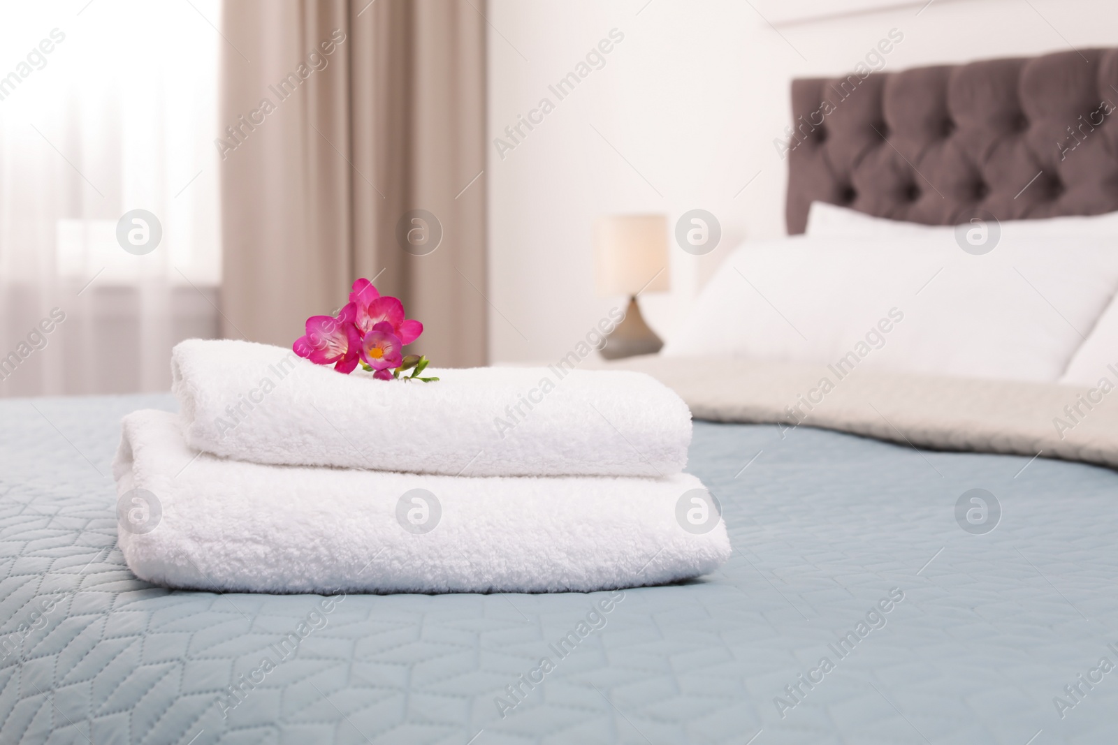 Photo of Stack of fresh towels with flowers on bed in hotel room