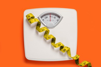 Photo of Bathroom scale and measure tape on orange background, top view