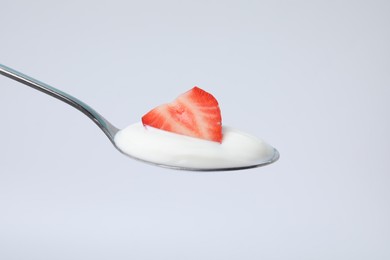 Photo of Delicious natural yogurt with fresh strawberry in spoon on light background