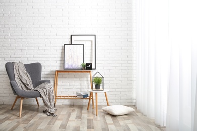 Stylish living room interior with comfortable armchair near brick wall. Space for text