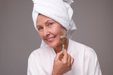 Photo of Woman massaging her face with jade roller on grey background