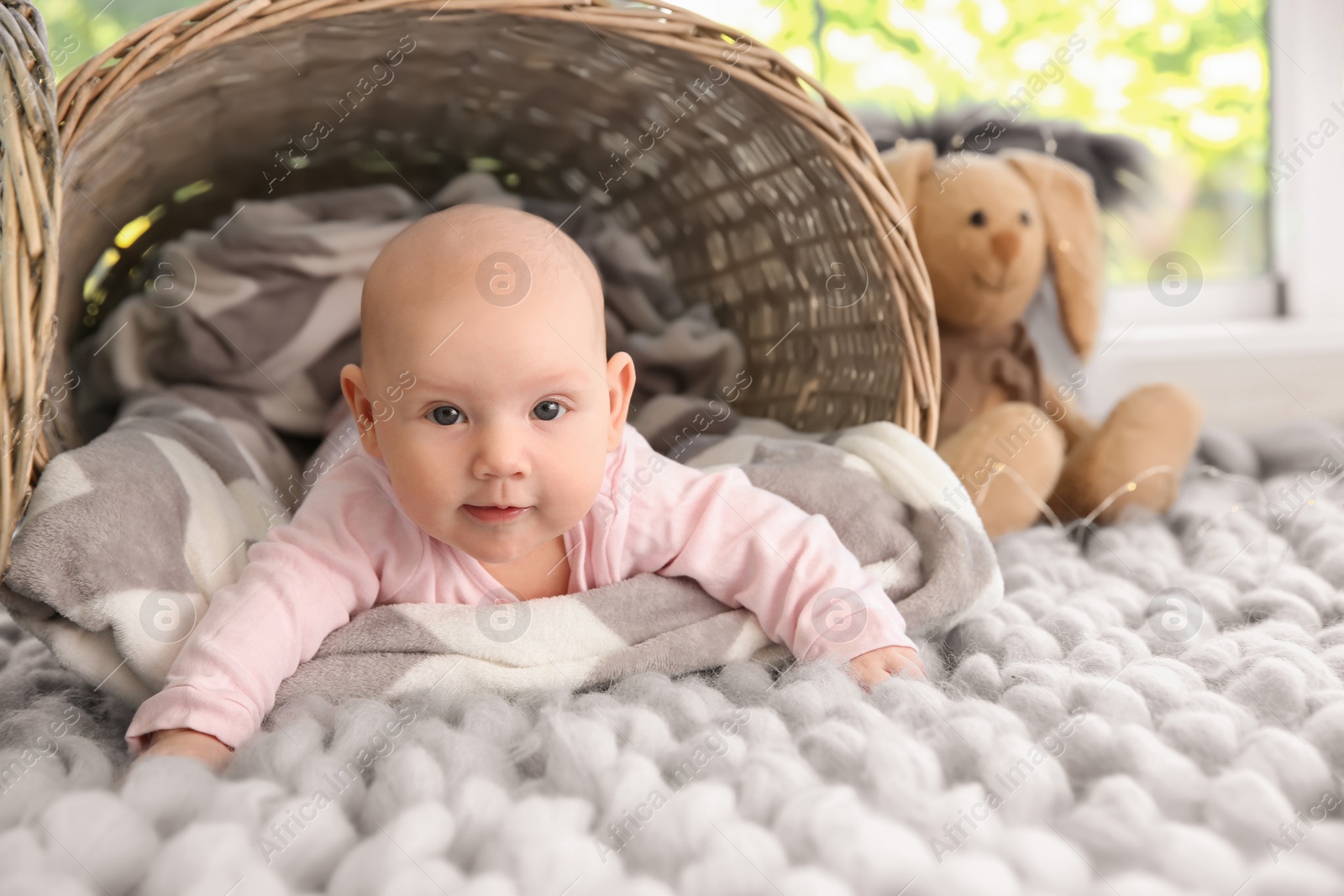 Photo of Adorable baby girl lying on soft plaid near wicker basket