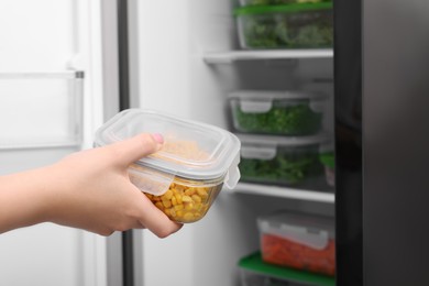 Photo of Woman putting container with tasty corn kernels into fridge, closeup. Food storage