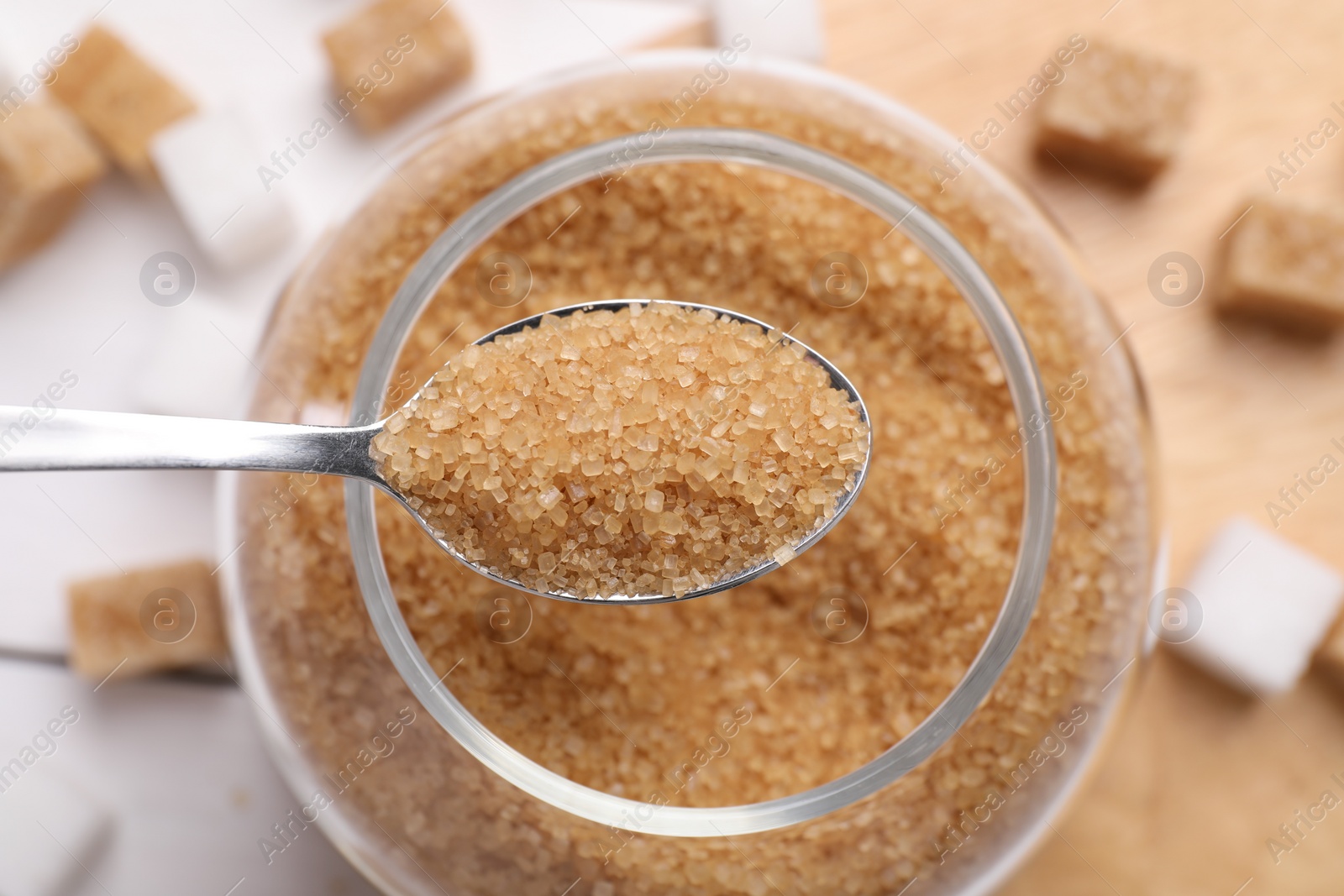 Photo of Spoon with brown sugar above jar on table, top view