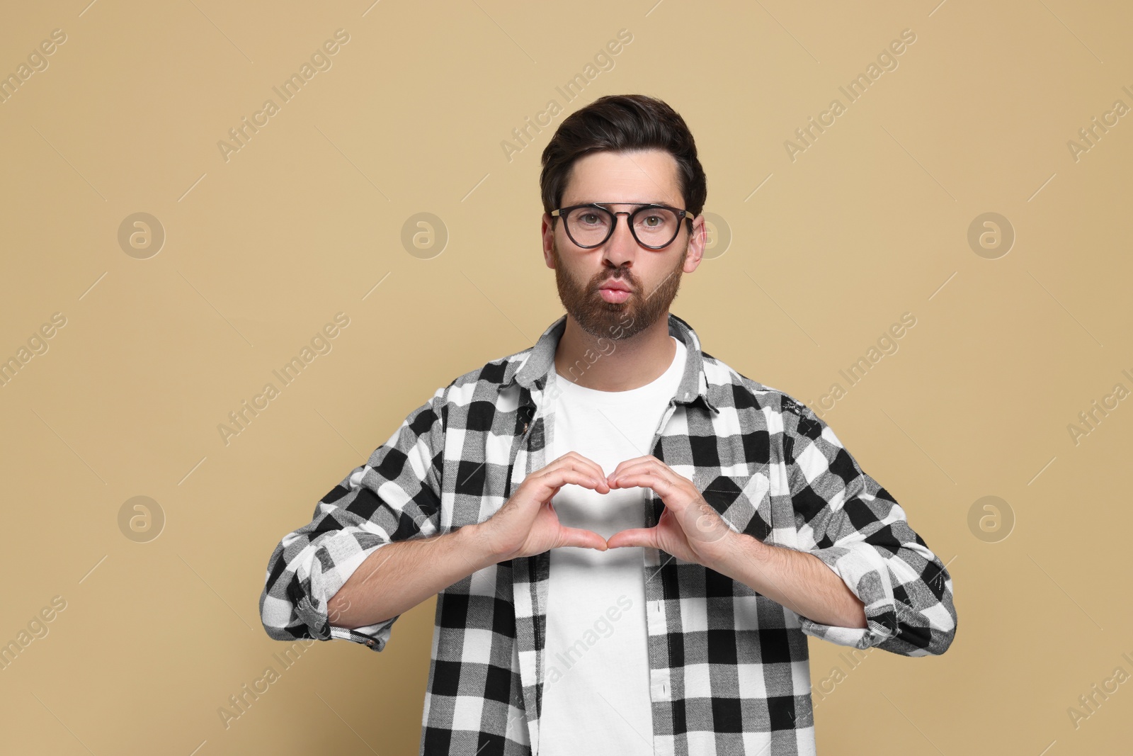 Photo of Handsome man making heart with hands and blowing kiss on beige background