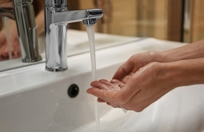 Photo of Woman washing hands under tap indoors, closeup