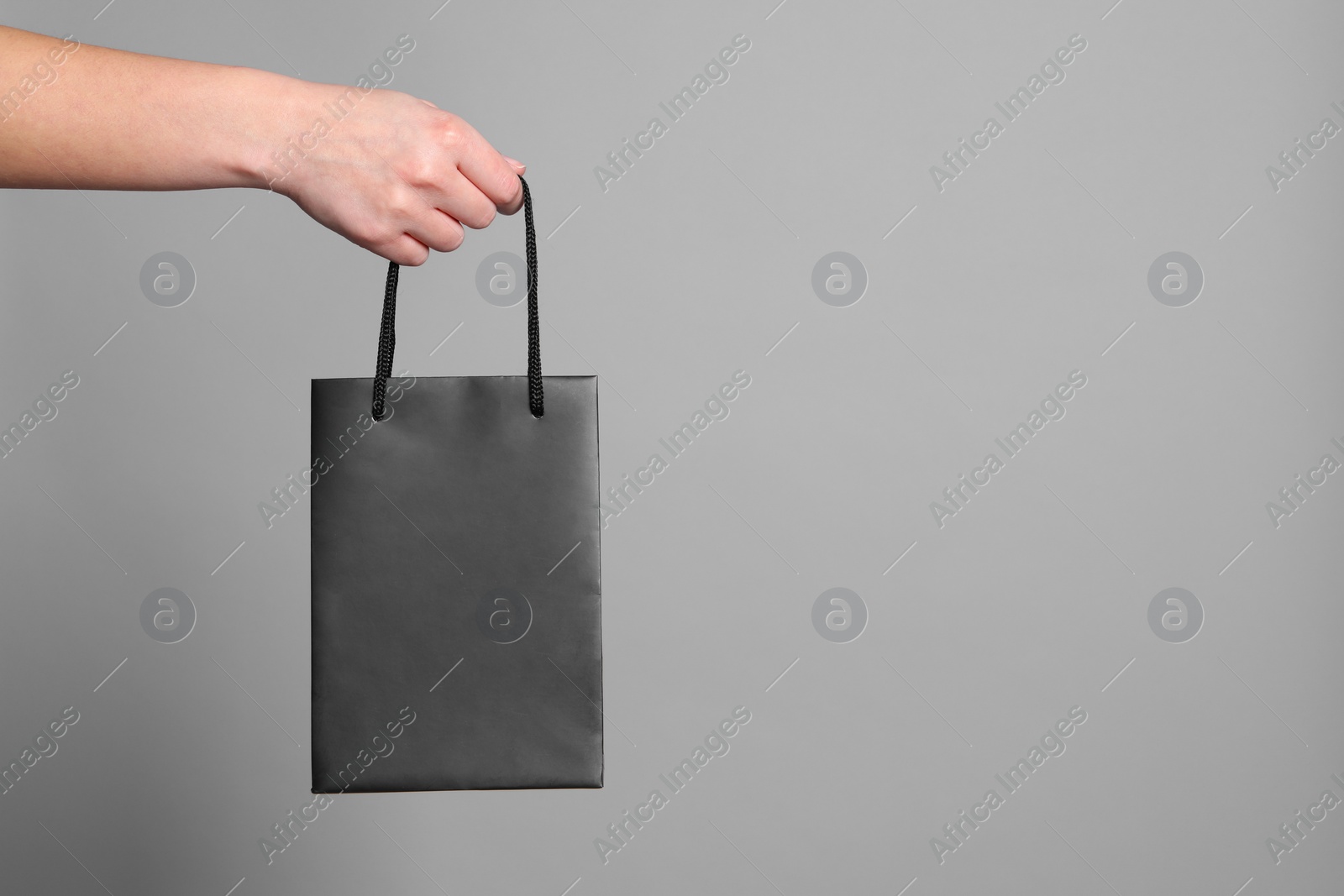 Photo of Woman holding paper shopping bag on grey background, closeup. Space for text