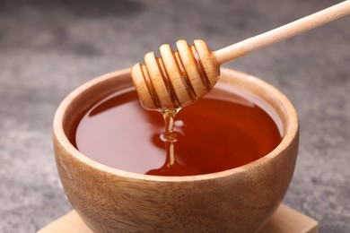 Photo of Pouring delicious honey from dipper into bowl on grey textured table, closeup