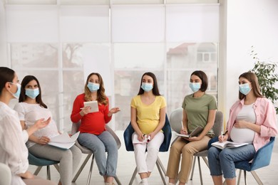 Photo of Group of pregnant women and midwife in protective masks at courses for expectant mothers indoors