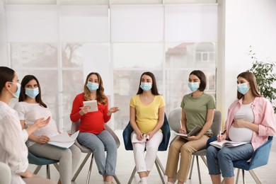 Group of pregnant women and midwife in protective masks at courses for expectant mothers indoors