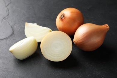 Photo of Whole and cut onions on black textured table