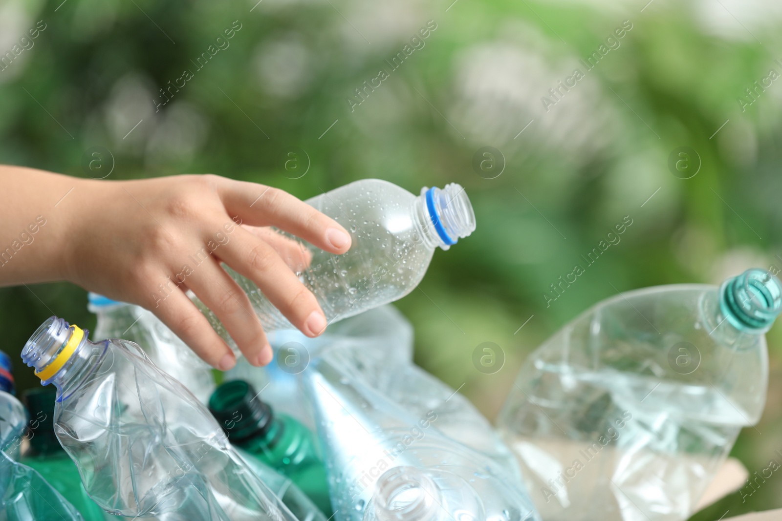 Photo of Woman putting used plastic bottle into cardboard box on blurred background, closeup. Recycling problem