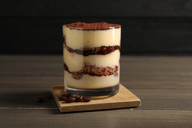 Delicious tiramisu in glass and coffee beans on wooden table, closeup