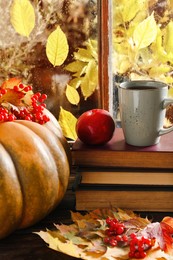 Photo of Stack of books, cup with aromatic tea, pumpkin and dry leaves on wooden windowsill indoors. Autumn atmosphere