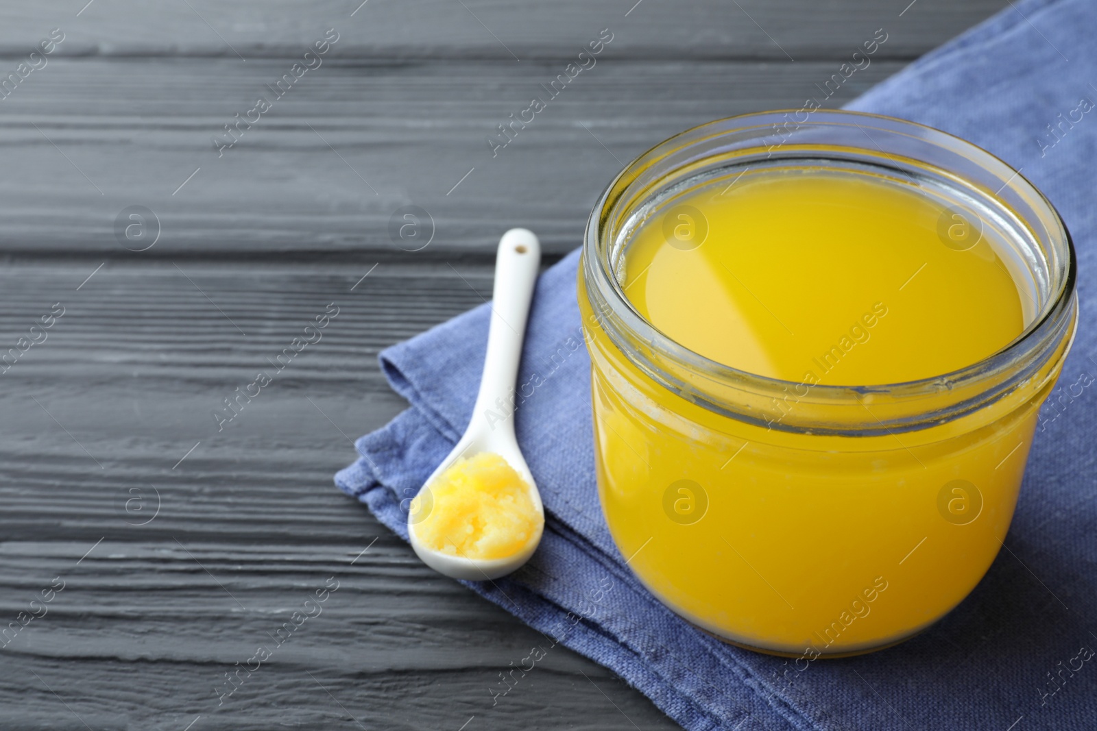 Photo of Glass jar and spoon of Ghee butter on grey wooden table, closeup. Space for text