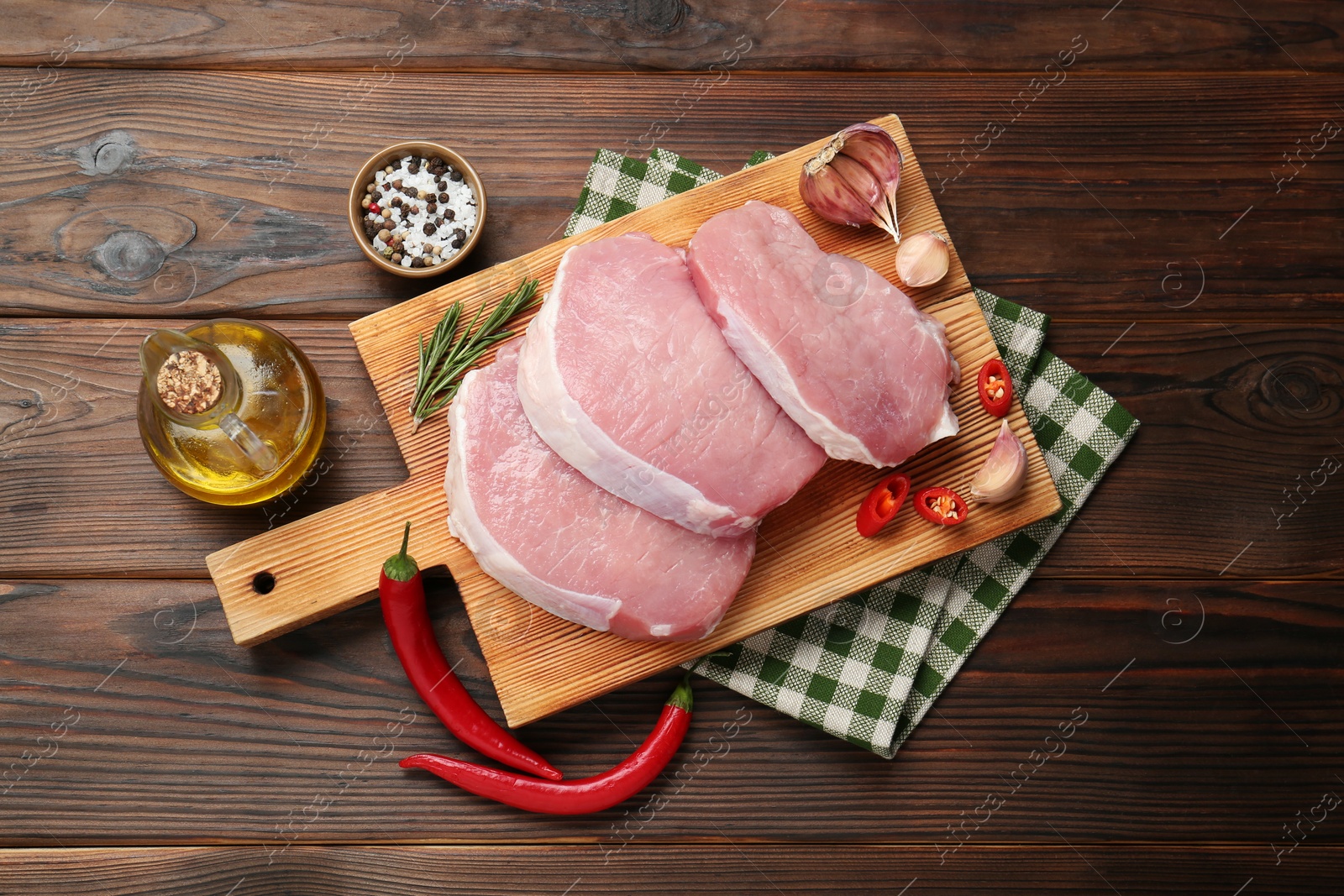 Photo of Pieces of raw pork meat, chili pepper, oil and spices on wooden table, flat lay