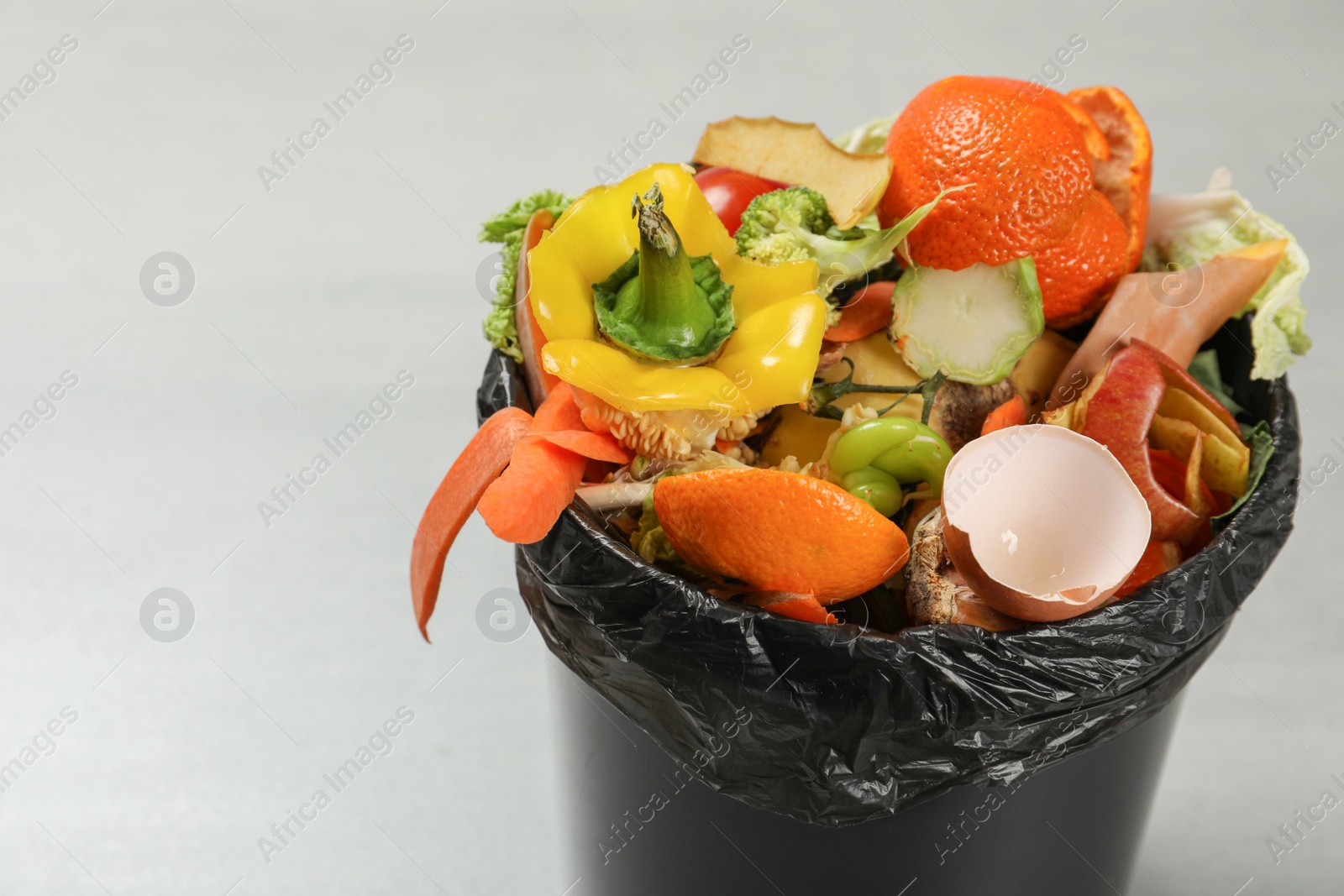 Photo of Trash bin with organic waste for composting on light background, closeup