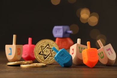 Photo of Dreidels with Jewish letters and coins on wooden table against blurred festive lights, selective focus. Traditional Hanukkah game