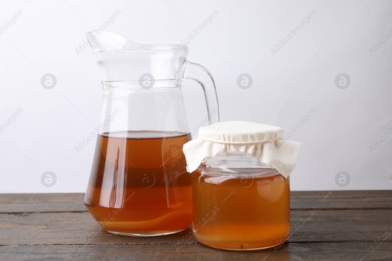 Photo of Homemade fermented kombucha in glass jar and jug on wooden table