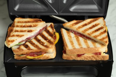 Photo of Modern grill maker with sandwiches on white table, closeup
